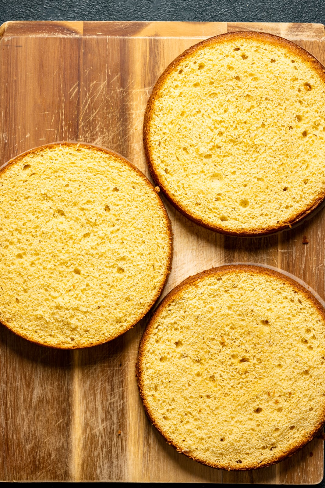 Baked cake layers placed on a brown cutting board. 