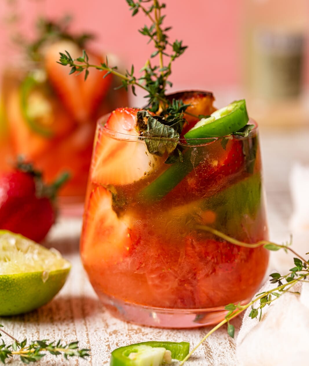 Spicy Grapefruit Jalapeño "Paloma" Mocktail in a small glass with halved strawberries, jalapeno slices, and thyme