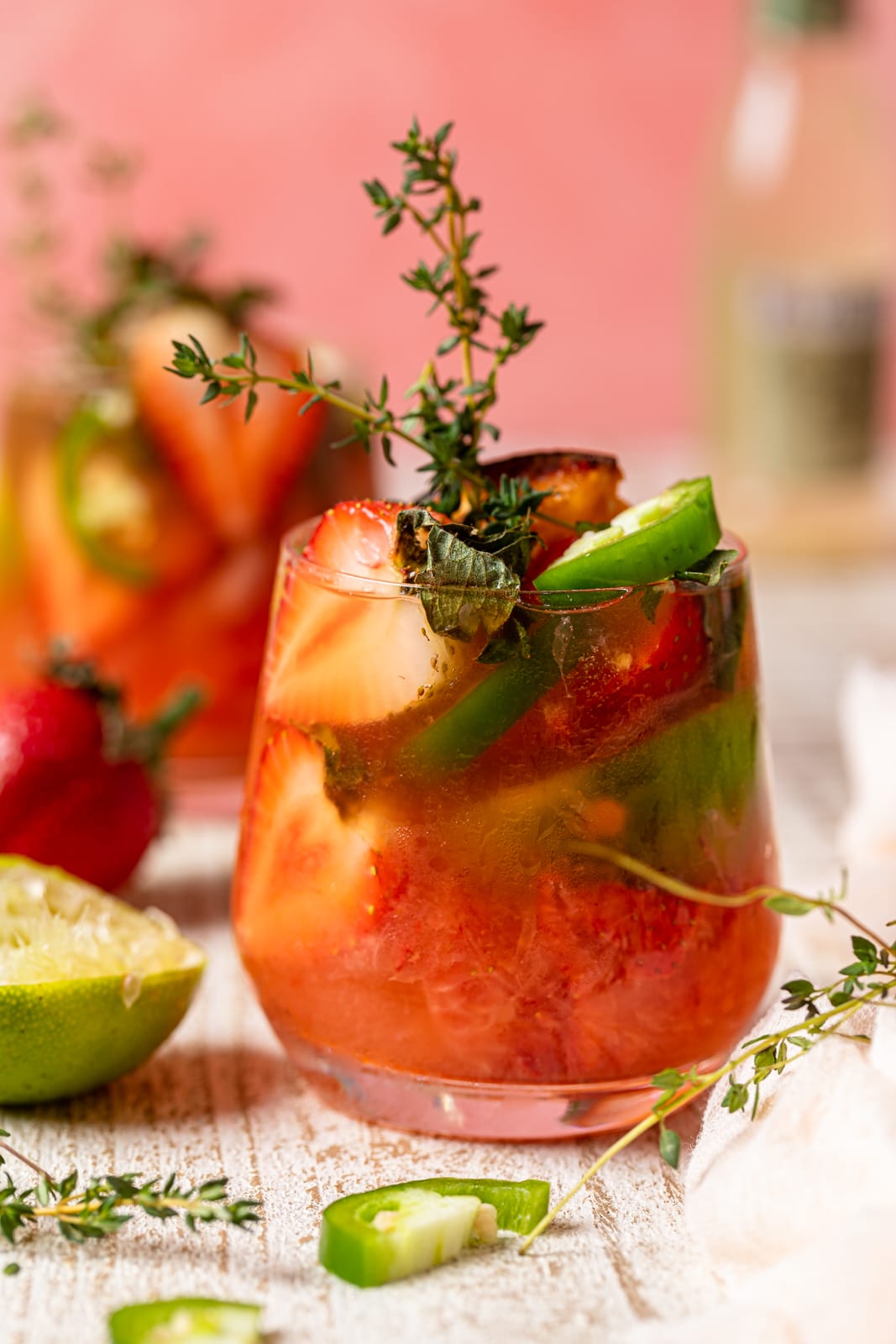 Spicy Grapefruit Jalapeño \"Paloma\" Mocktail in a small glass with halved strawberries, jalapeno slices, and thyme