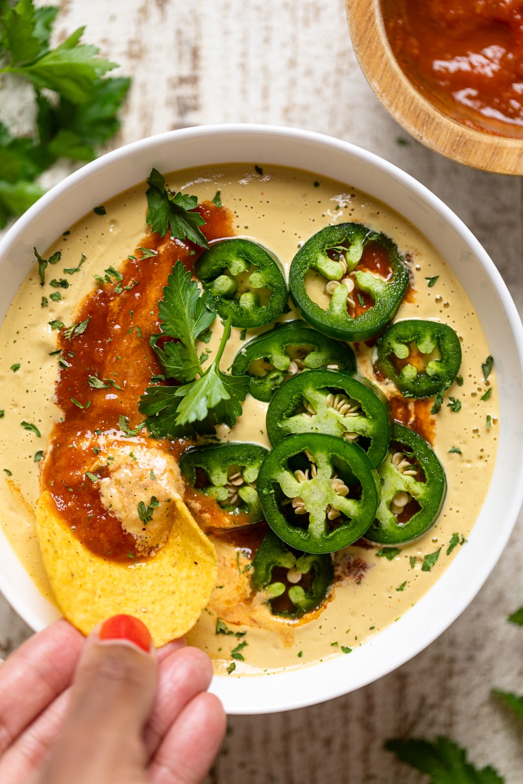 Hand dipping a chip into a bowl of Vegan Jalapeno Queso Dip