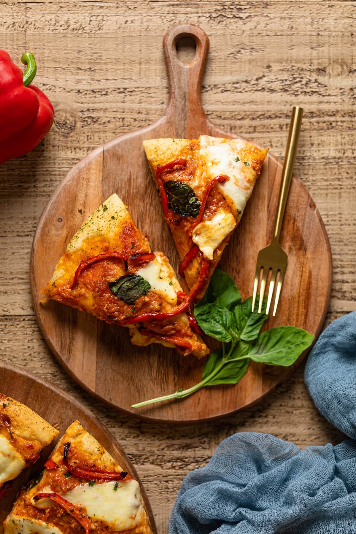 Two slices of Vodka Pizza on a wooden board with a fork and basil leaves