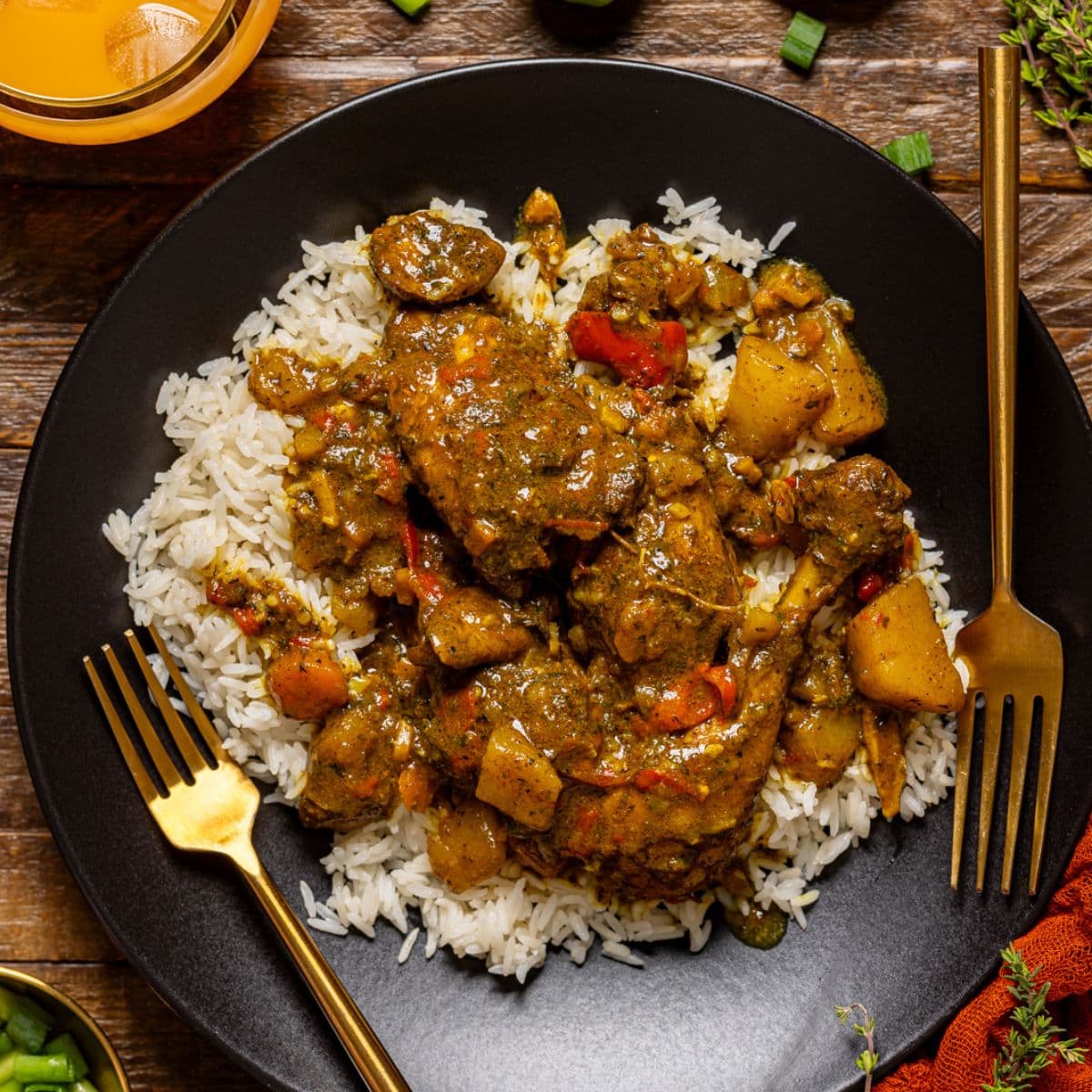 Curry chicken in a black plate with two forks and a side of drink.