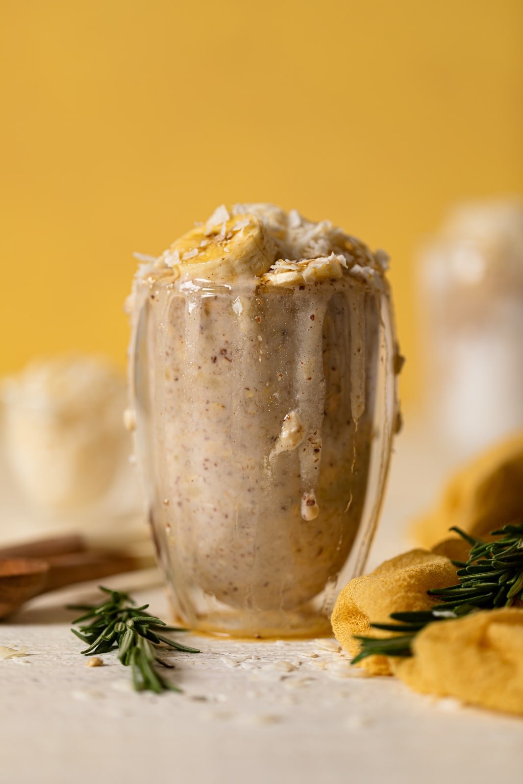 Overflowing glass of Banana Coconut Overnight Oats topped with banana slices