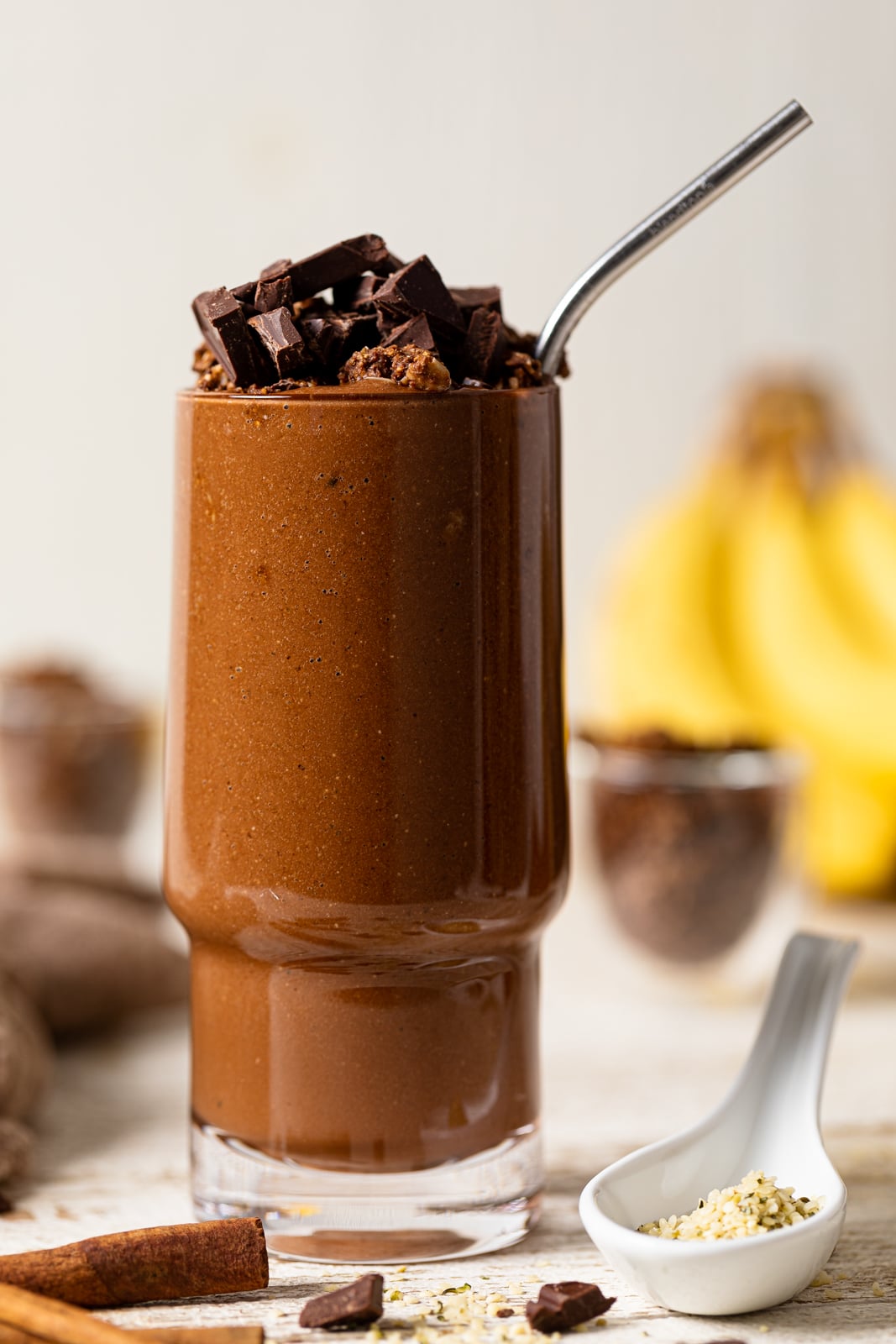 Chocolate Banana Smoothie with Espresso in a tall glass topped with chocolate pieces and with a straw