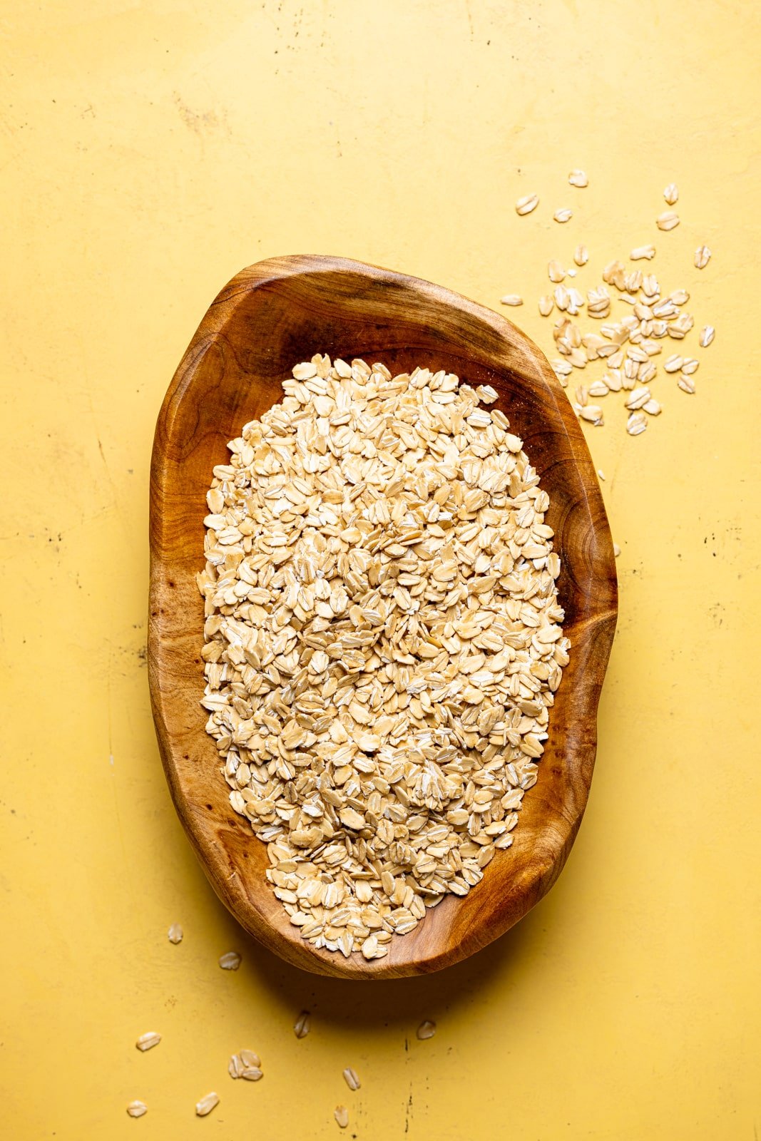 Rolled oats in a wood bowl on a yellow table.