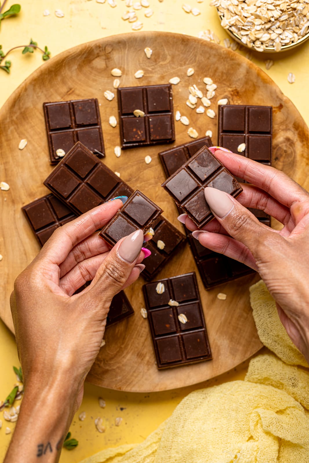 chocolate bars being held in hands with a brown wood plate in the background.
