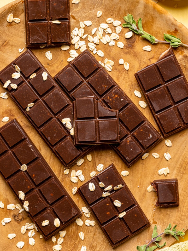 Chocolate bars on a brown wood plate with garnish of oats and herbs broken into pieces.