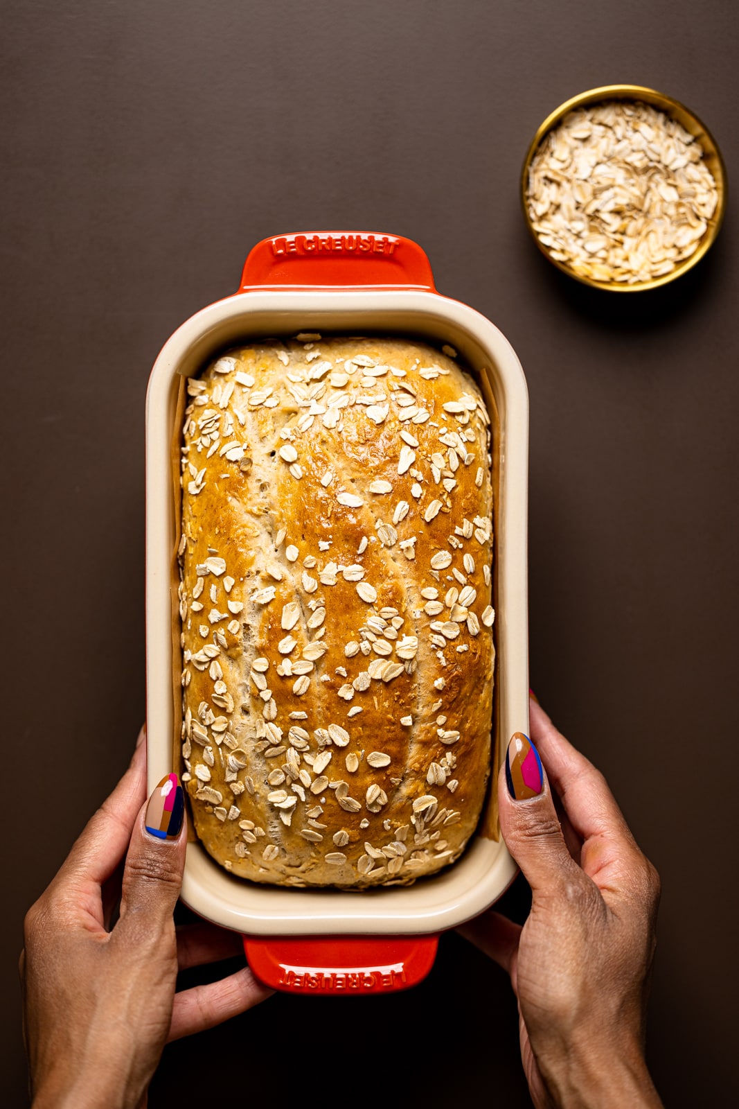 Baked bread in a red loaf pan on a brown table.