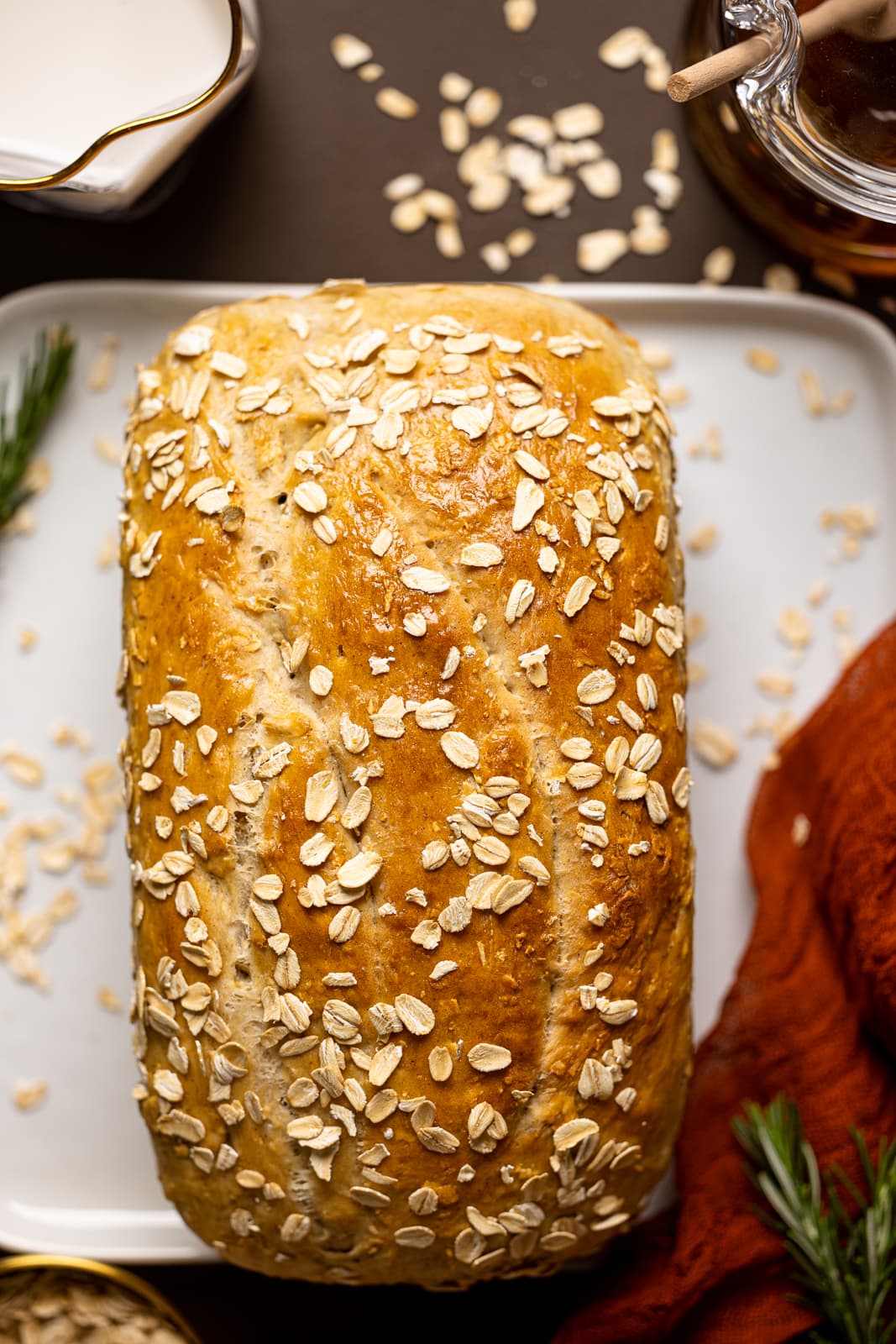 Baked bread on a white plate on a brown table with red napkin with a glass of milk and honey.