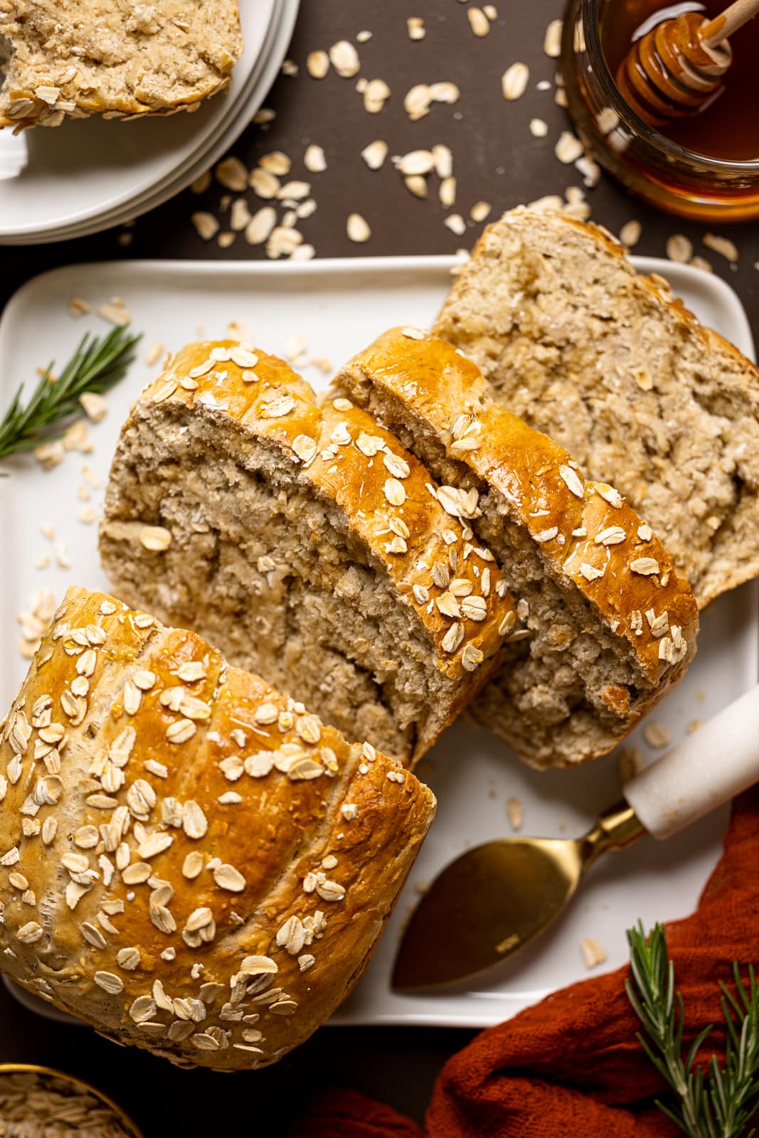 Sliced honey oat bread on a white plate on a brown table with red napkin and oats.