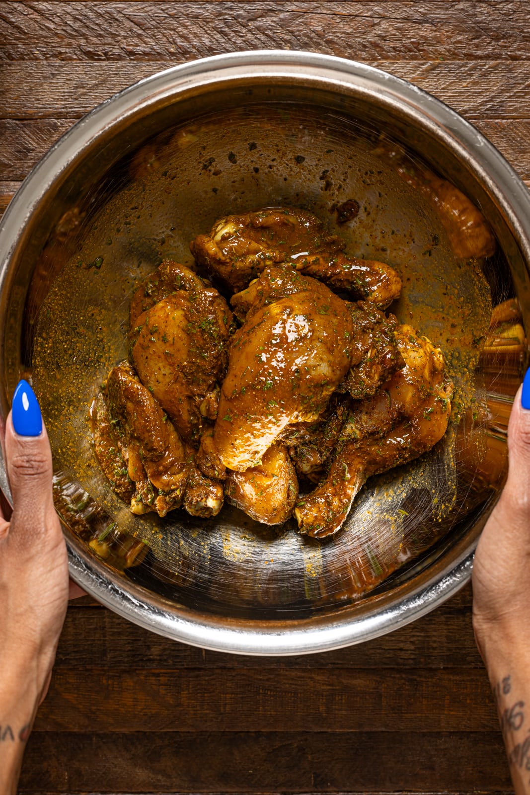 Marinated chicken in a silver bowl being held.