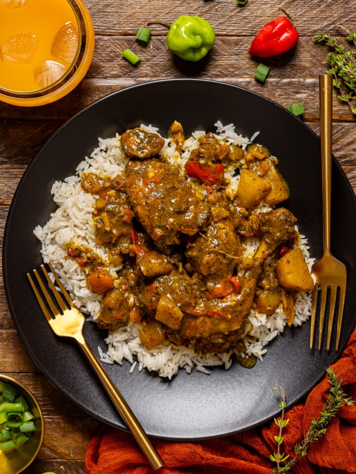 Curry chicken in a black plate with two forks and a side of drink.