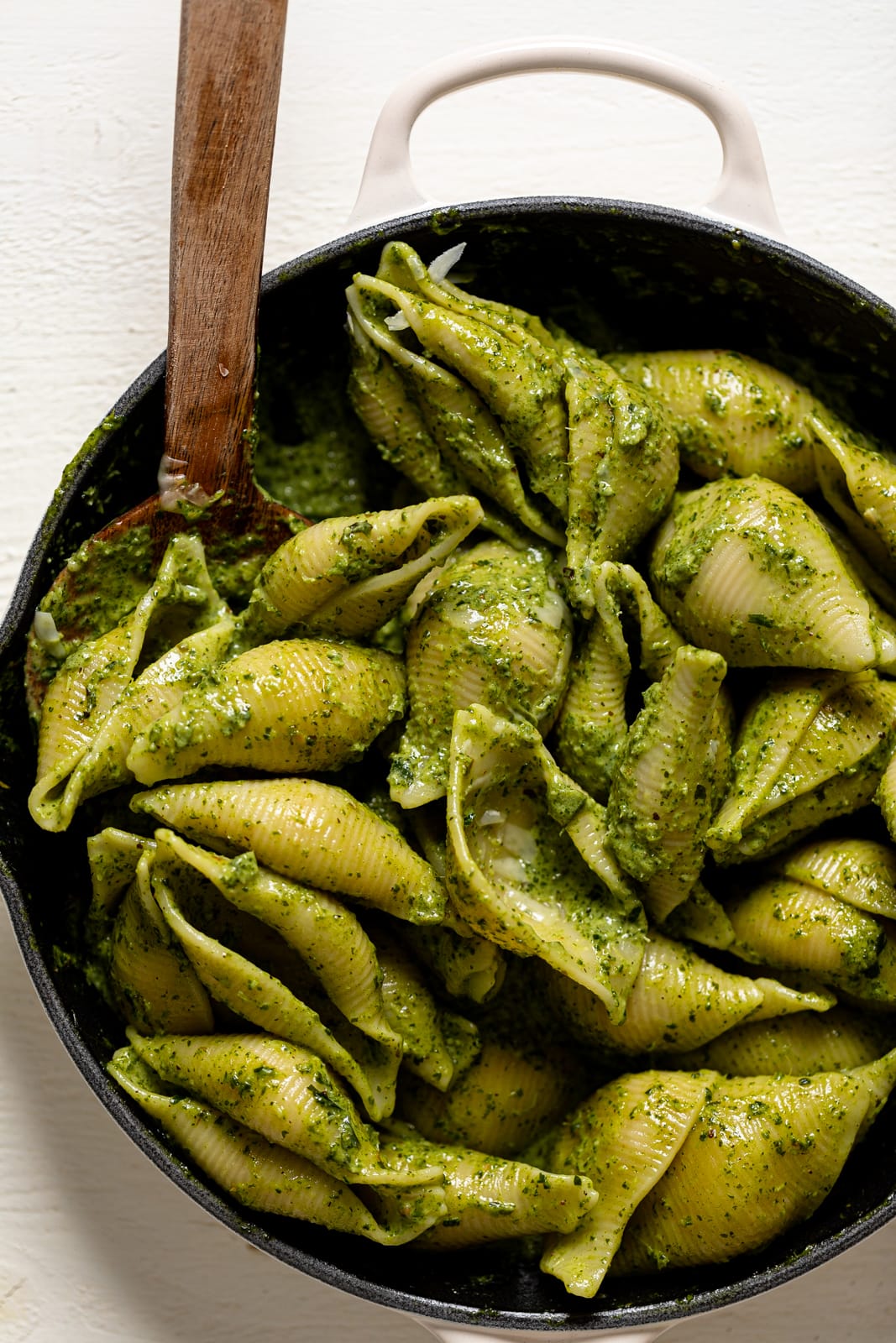 Closeup of a wooden spoon stirring a skillet of Creamy Roasted Garlic Kale Pasta with Parmesan