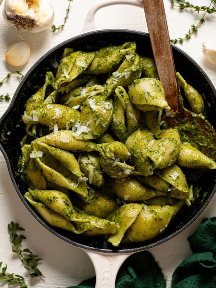 Wooden spoon stirring a skillet of Creamy Roasted Garlic Kale Pasta with Parmesan