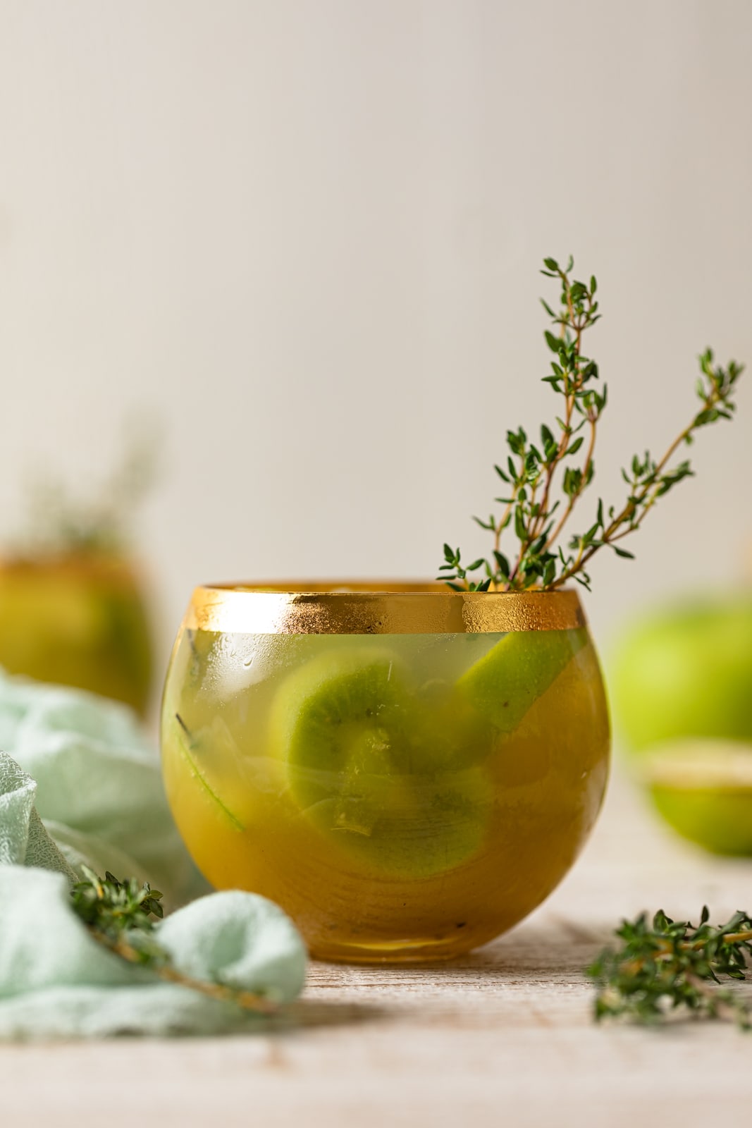 Green Goddess Mocktail with thyme in a gold-rimmed glass