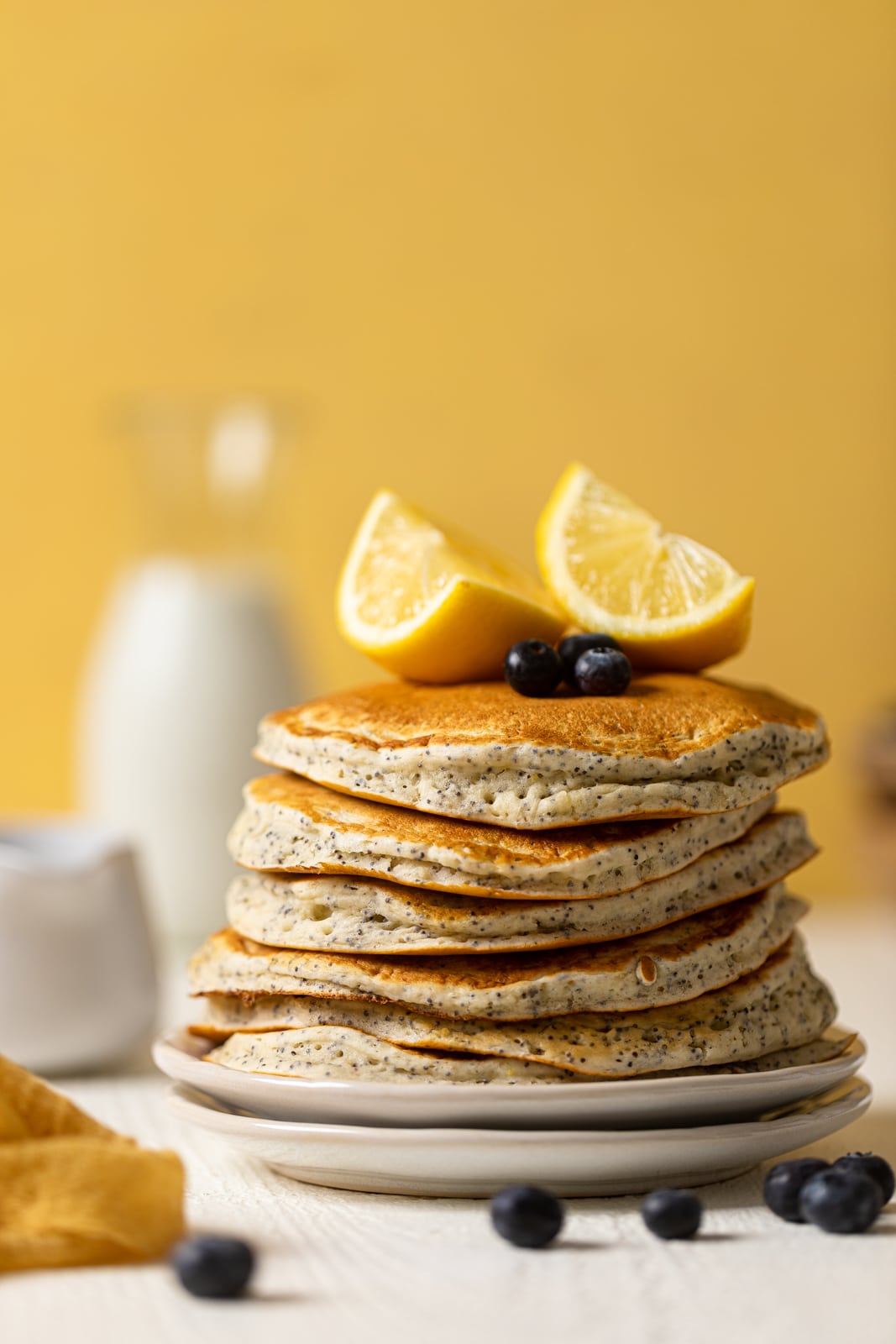 Stack of Vegan Lemon Poppyseed Pancakes topped with lemon wedges and blueberries