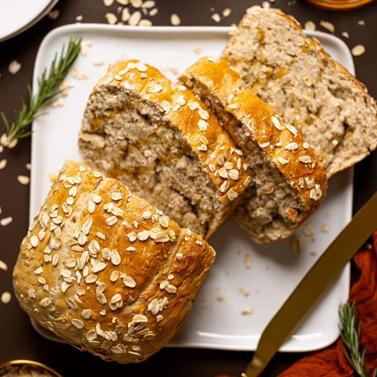 Bread sliced on a white plate on a brown table with red napkin and oats.