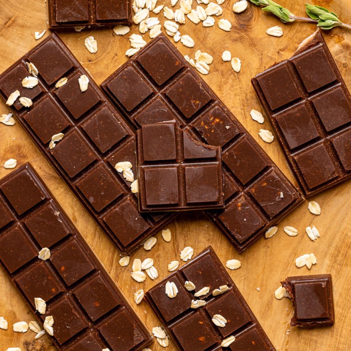 Chocolate bars on a brown wood plate with garnish of oats and herbs broken into pieces.