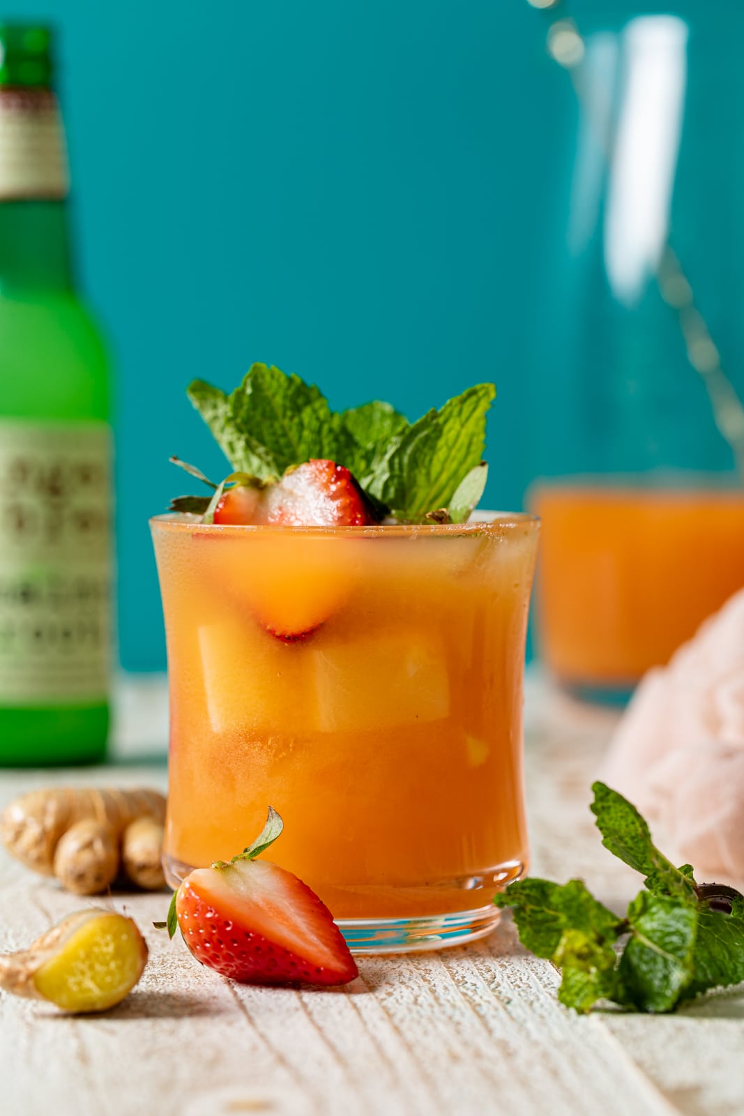 Glass of Jamaican Rum Punch Mocktail surrounded by strawberries and ginger