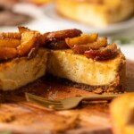 Cheesecake on a brown cutting board with peaches and a fork.