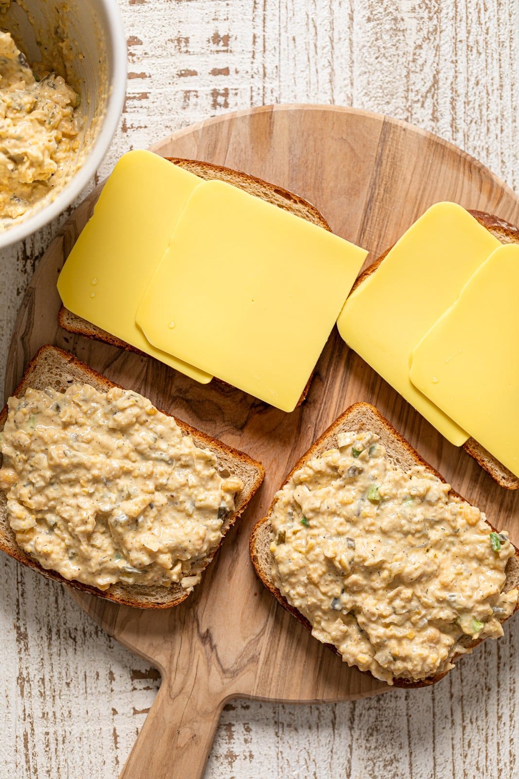 Two slices of bread full of vegan \"tuna\" with two slices of bread topped with slices of vegan cheese