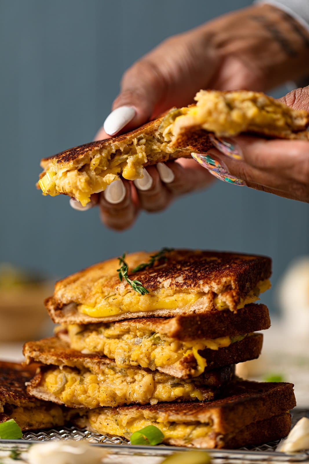 Hand grabbing a Vegan Chickpea Tuna Melt Sandwich from the top of a stack