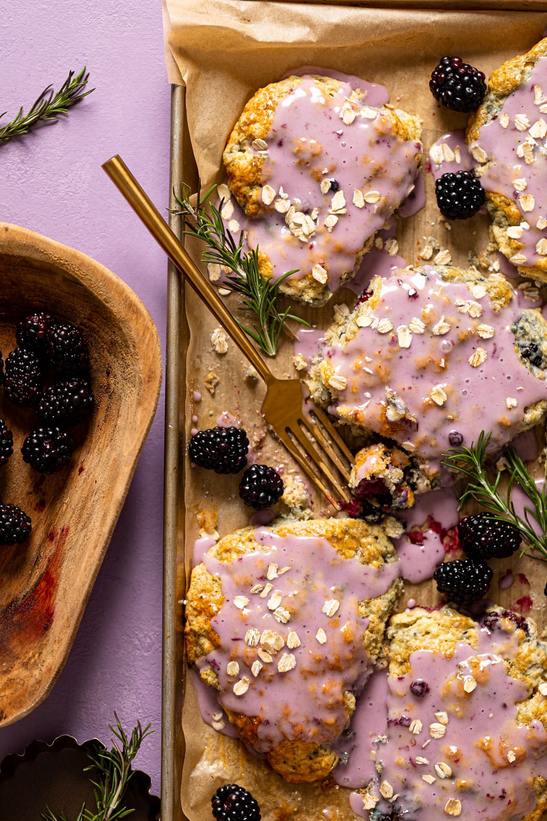 Sheet pan of Blackberry White Chocolate Oatmeal Scones next to a wooden bowl of blackberries