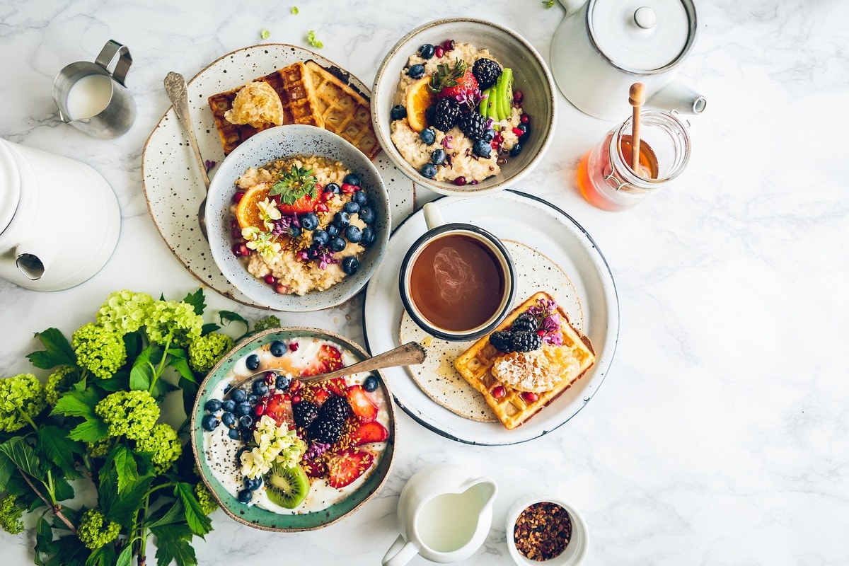 Overhead shot of a large breakfast spread including colorful, fruity oatmeal, waffles, and coffee