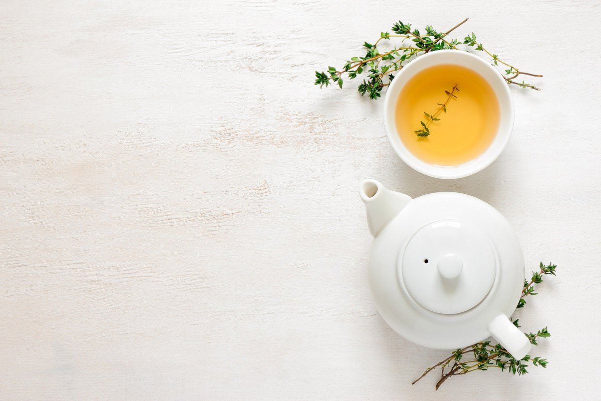 Overhead shot of a white tea pot, a white tea cup with tea, and thyme