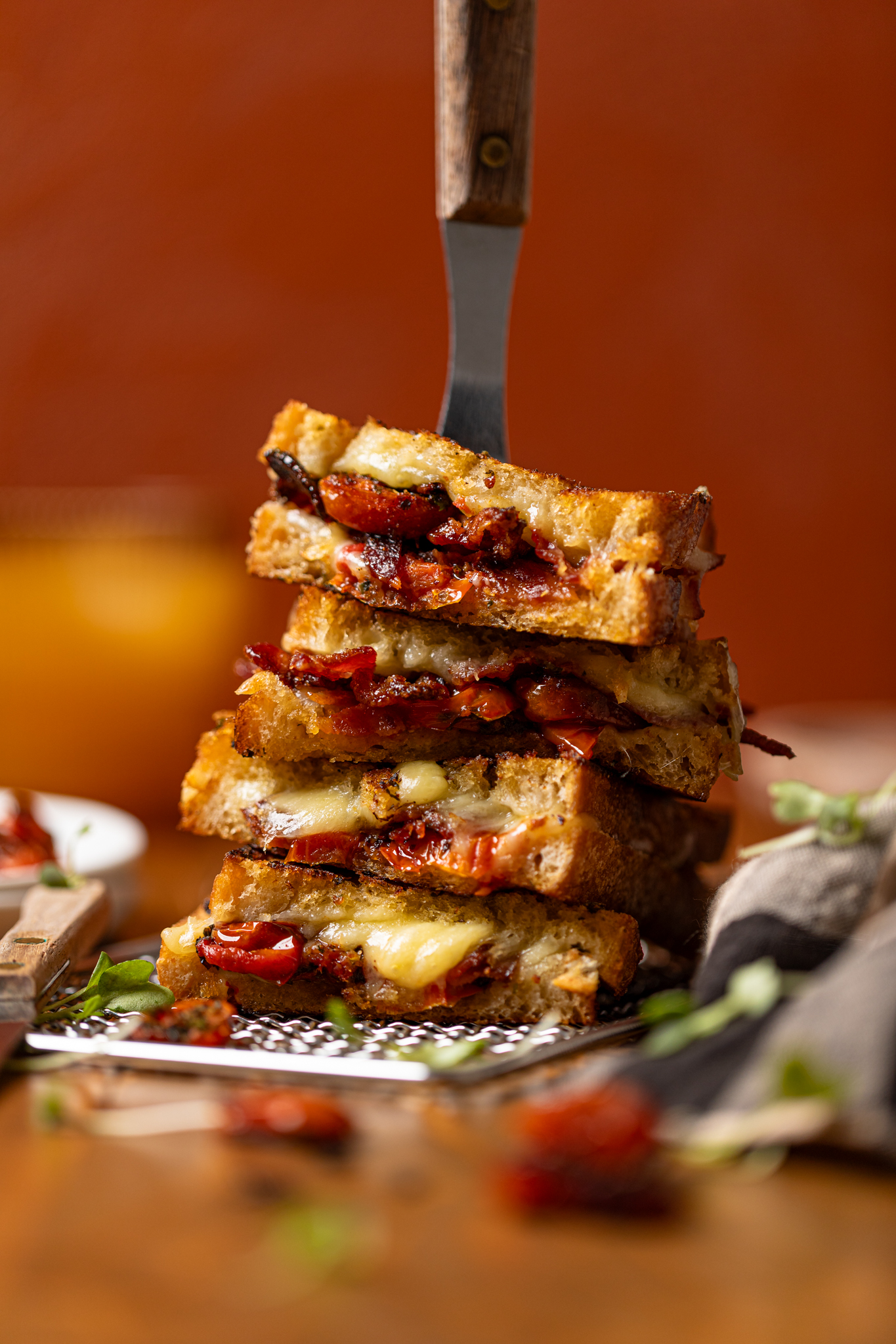 Forward shot of stacked grilled cheese sandwiches with a fork through the top with roasted tomatoes.