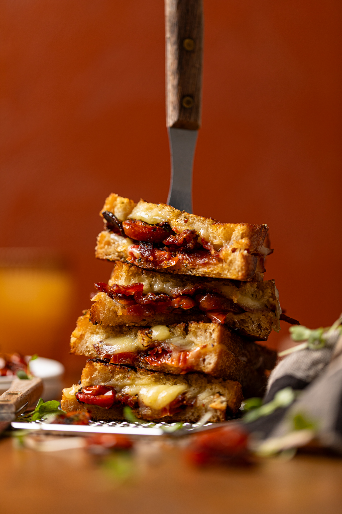 Forward shot of stacked grilled cheese sandwiches with a fork through the top with roasted tomatoes.
