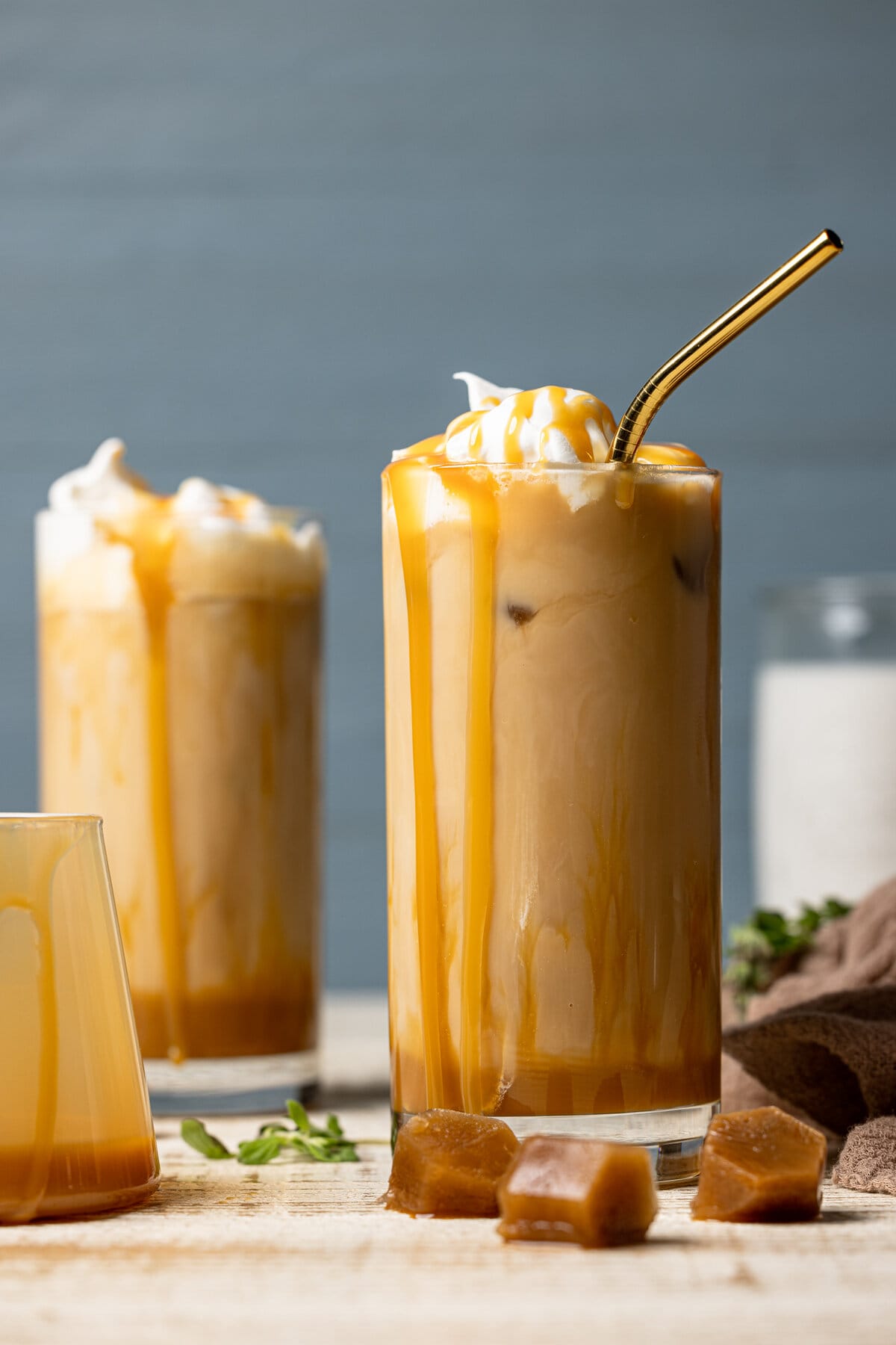 Two Iced Caramel Lattes with caramel dripping down the sides of the glasses, one with a straw