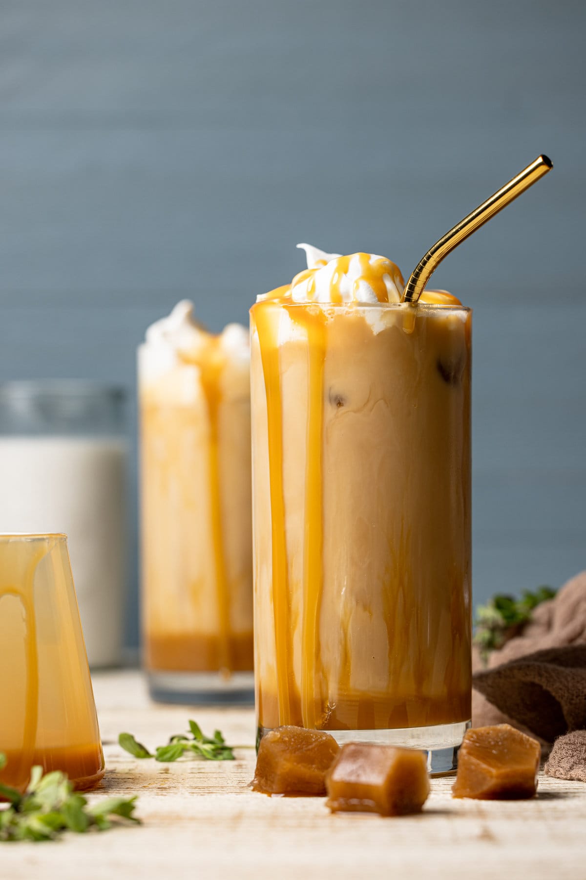 Two Iced Caramel Lattes with caramel dripping down the sides of the glasses, one with a straw