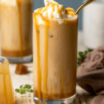 Closeup of an iced caramel latte with caramel dripping down the sides of the glass