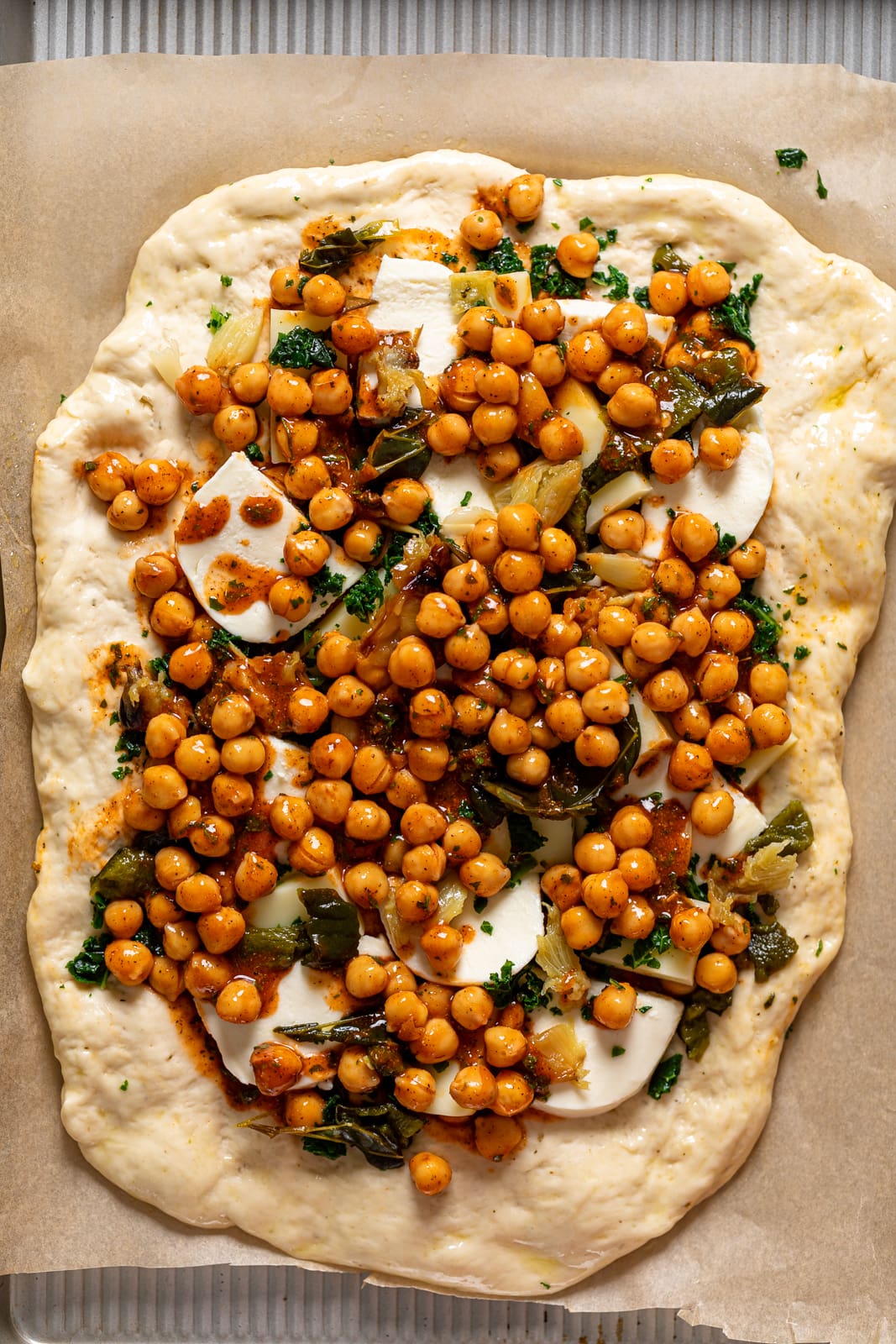 Uncooked Sheet Pan Roasted Garlic Buffalo Chickpea Pizza on parchment paper