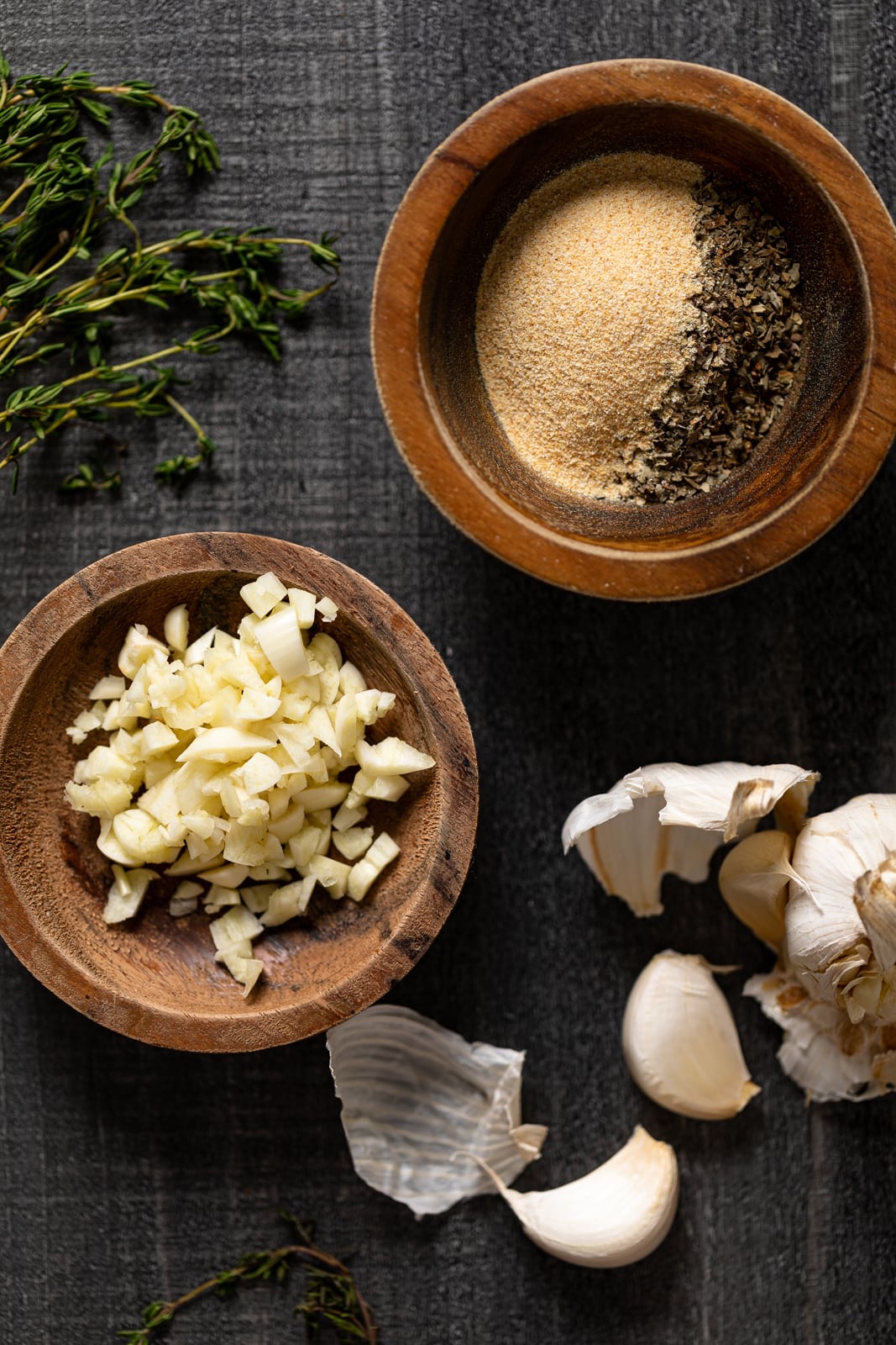 Bowl of minced garlic next to a bowl of spices and some thyme leaves