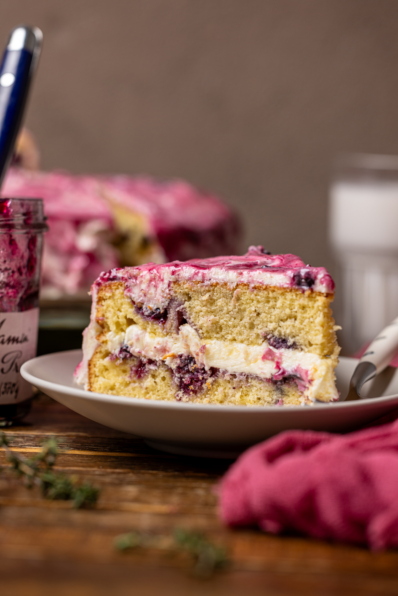An image of a slice of cake on a plate with milk, cake, and jam in the background. 
