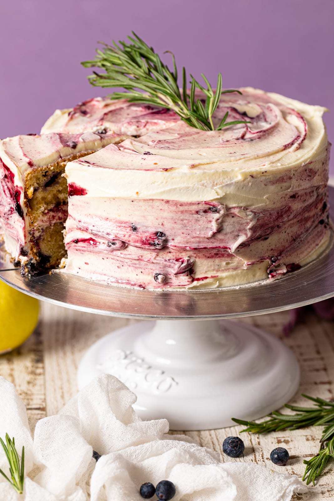 Lemon Blueberry Olive Oil Cake on an elevated platter with a slice pulled out