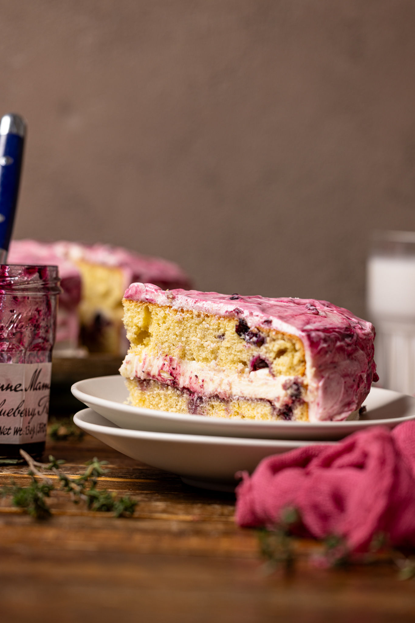 An image of a cake slice on a plate with cake and milk in background.