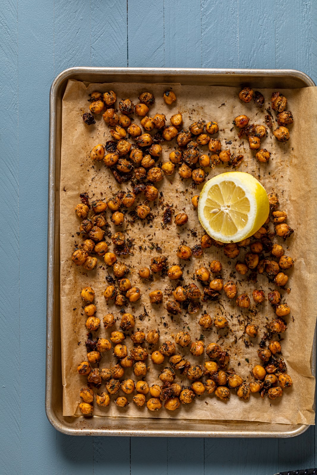 Sheet pan of seasoned, roasted chickpeas with a lemon half