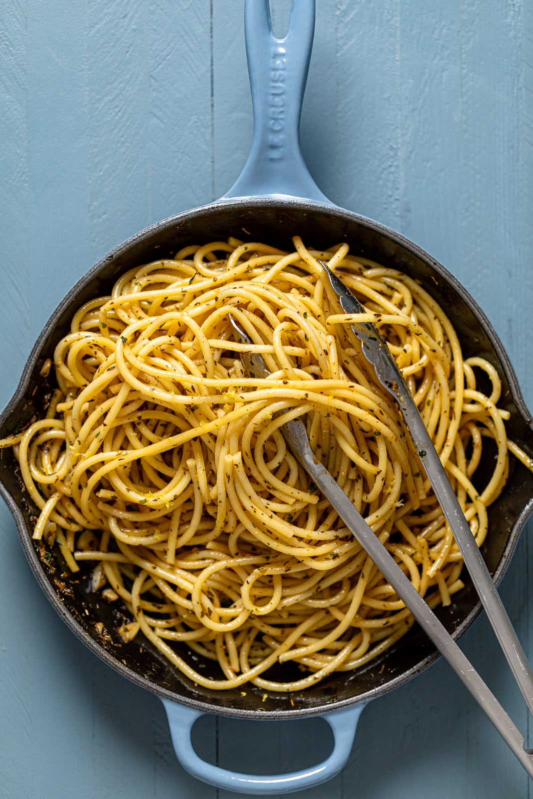 Tongs in a skillet of seasoned noodles