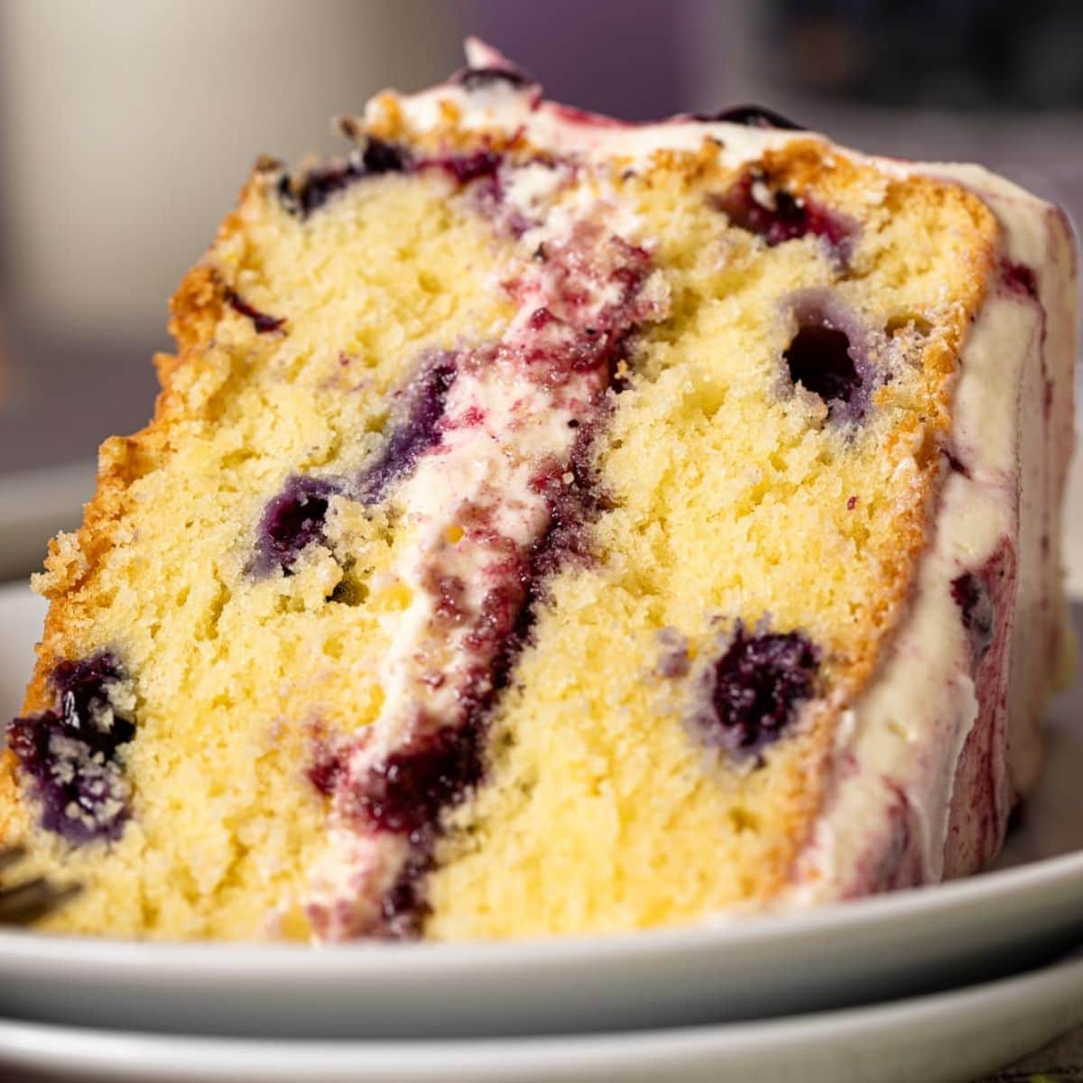 Up close shot of a slice of Lemon Blueberry Olive Oil cake on two white plates.