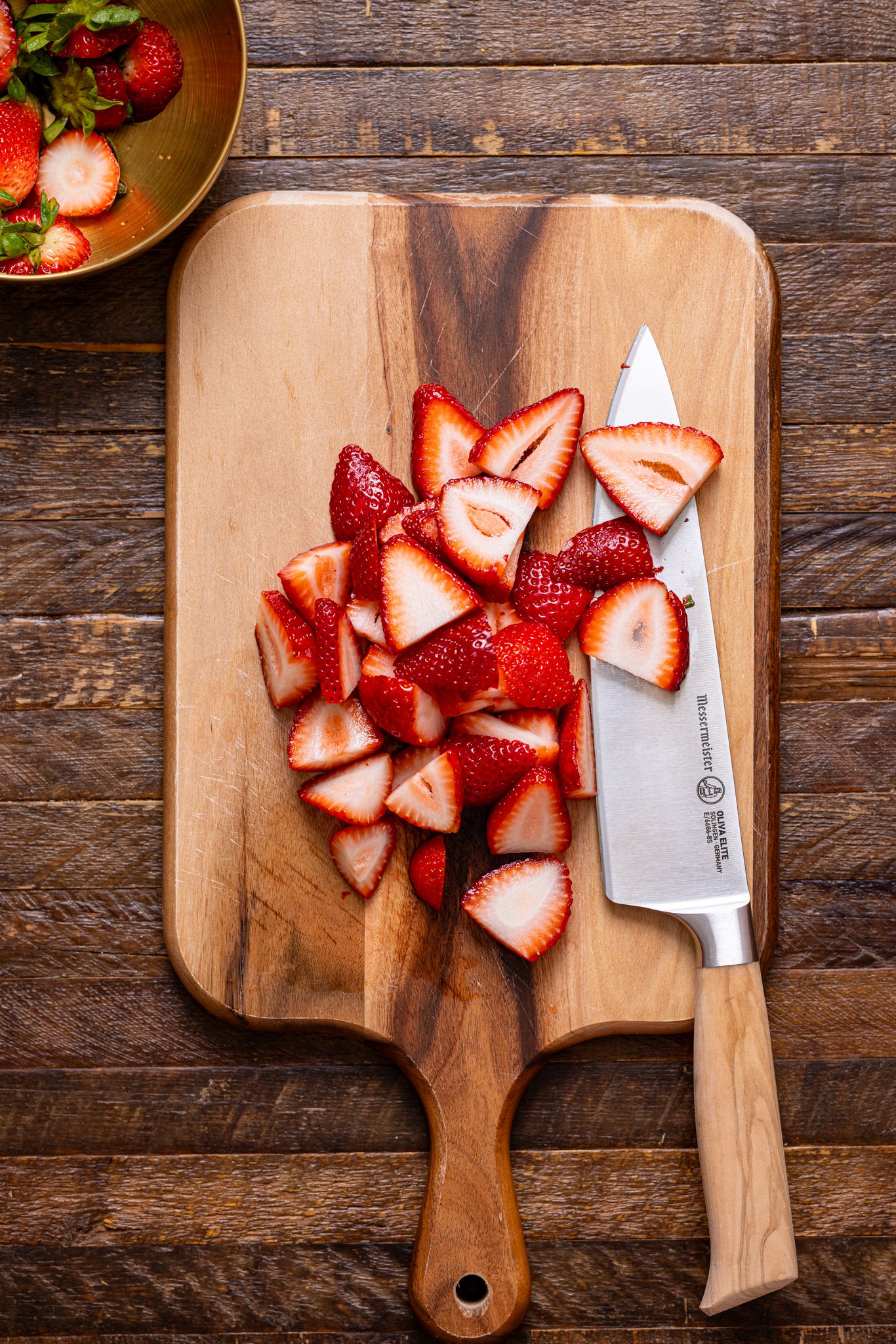 Chopped strawberries on a cutting board with a knife.
