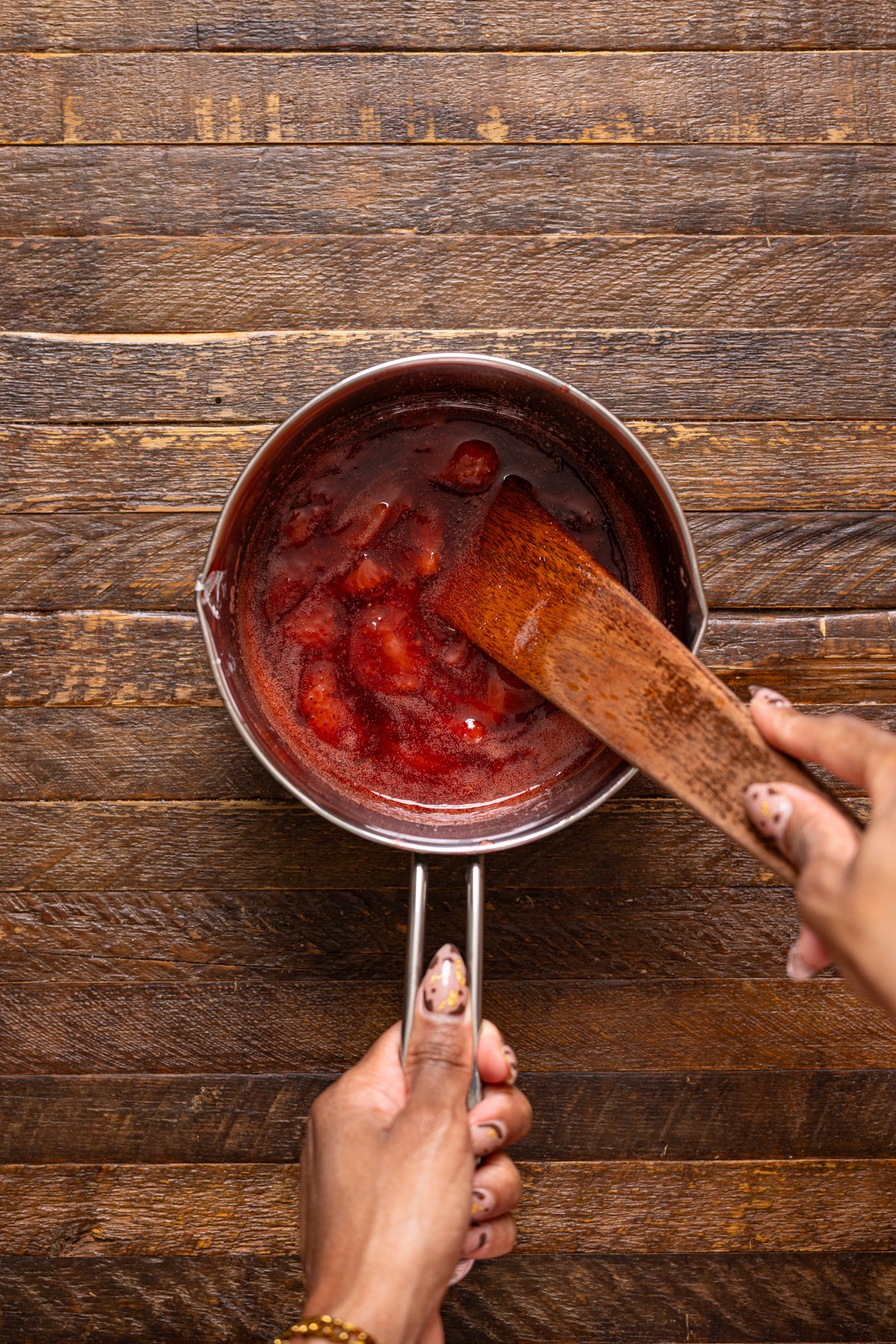 Strawberry sauce in a saucepan being stirred with a wooden spoon.