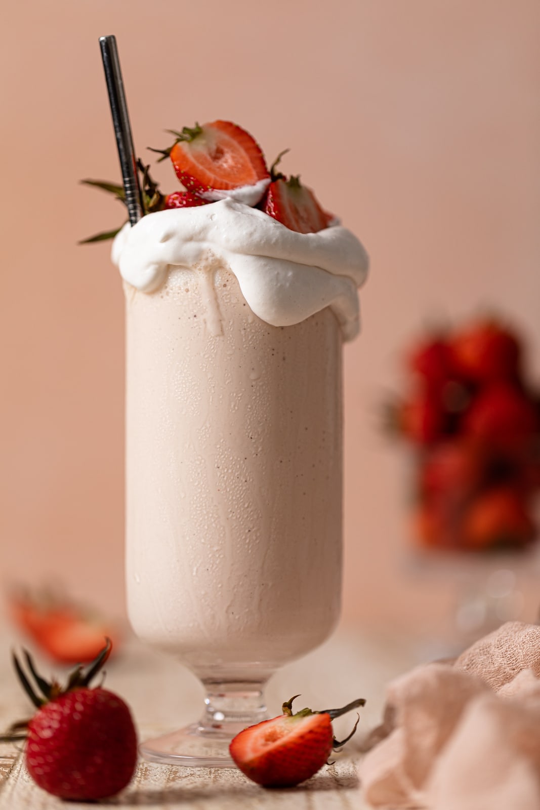 Glass overflowing with Dairy-Free Strawberry Milkshake with a straw