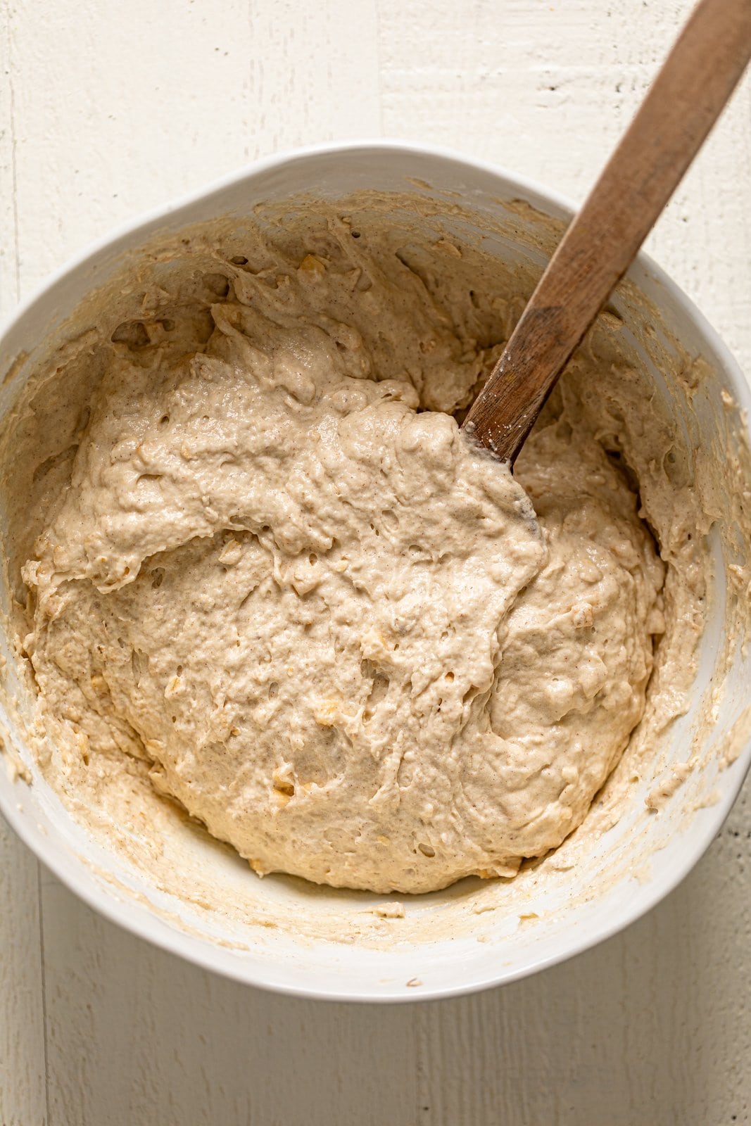 Wooden spoon stirring a bowl of Vegan Apple Oatmeal Sheet Cake batter