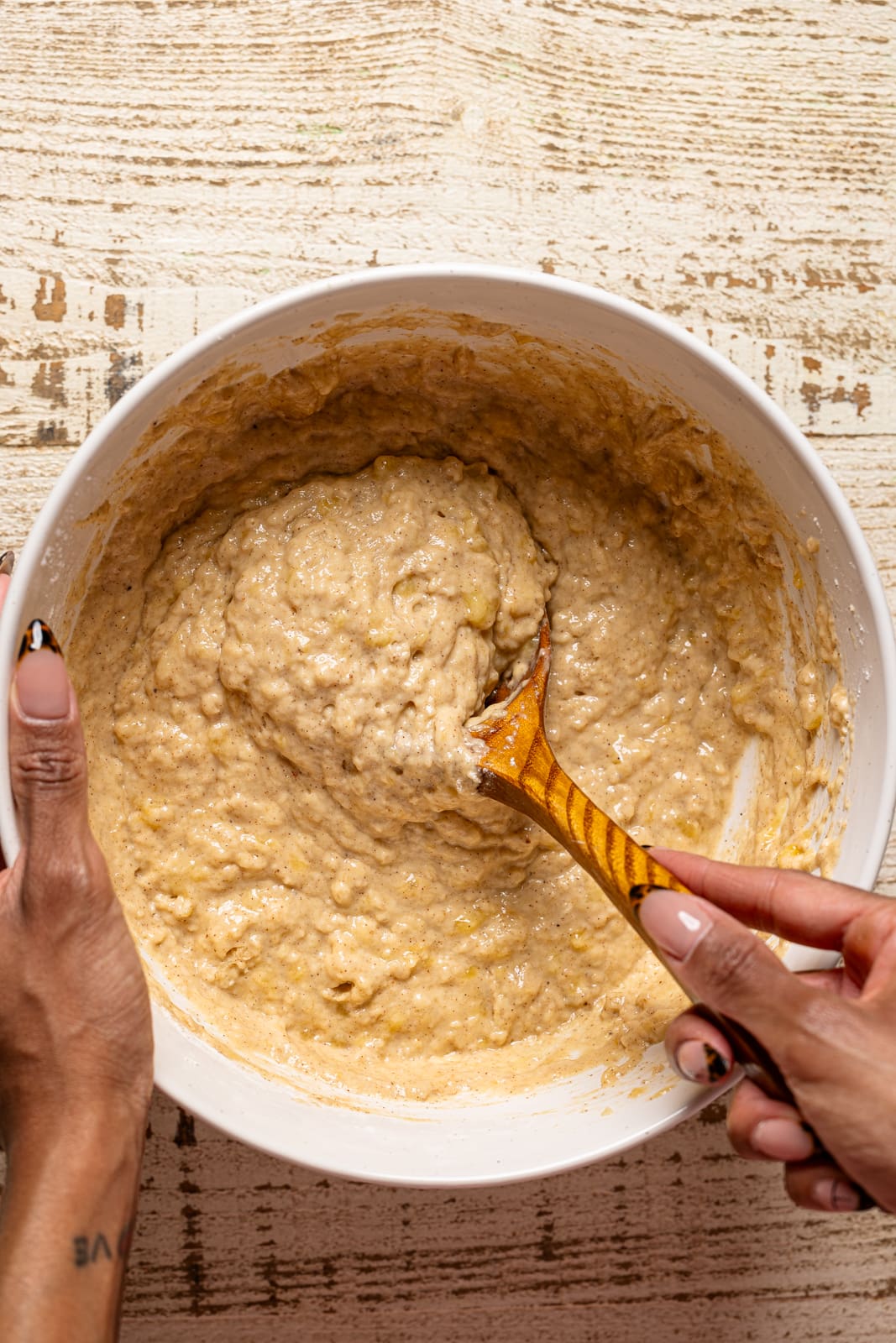 Bread batter being stirred in a white bowl with a wooden spoon.