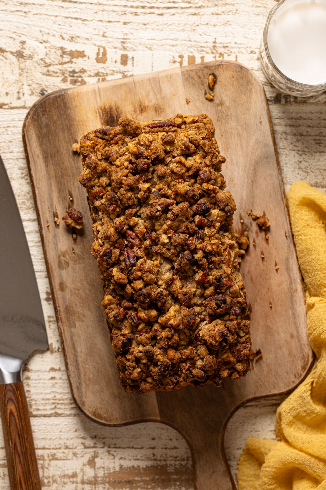 Overhead shot of banana bread with crumble topping on a cutting board with a knife.