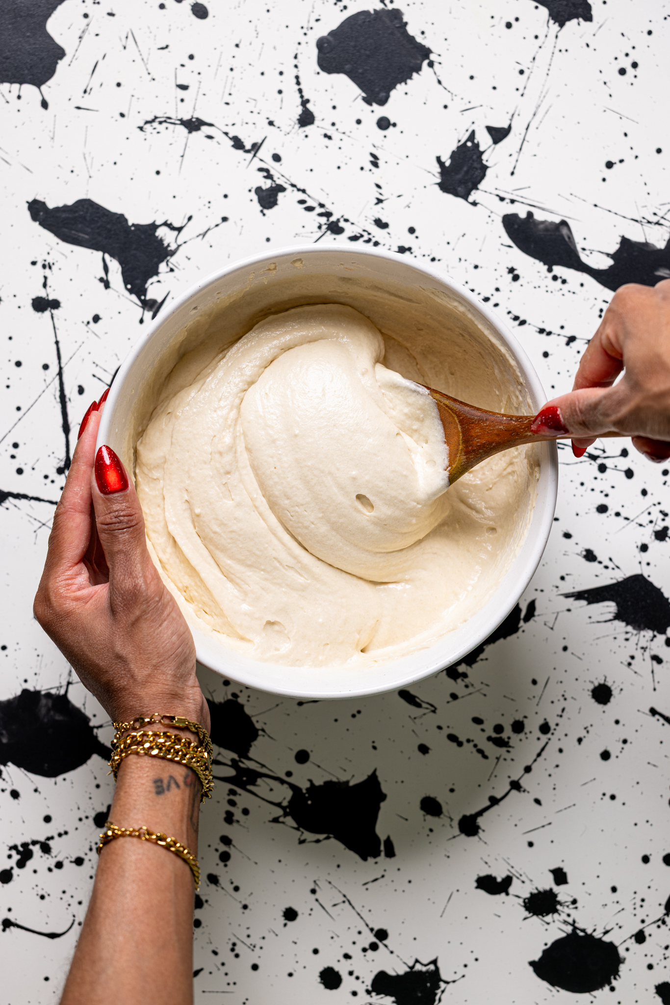Cake batter being mixed in a bowl being held by women hands.