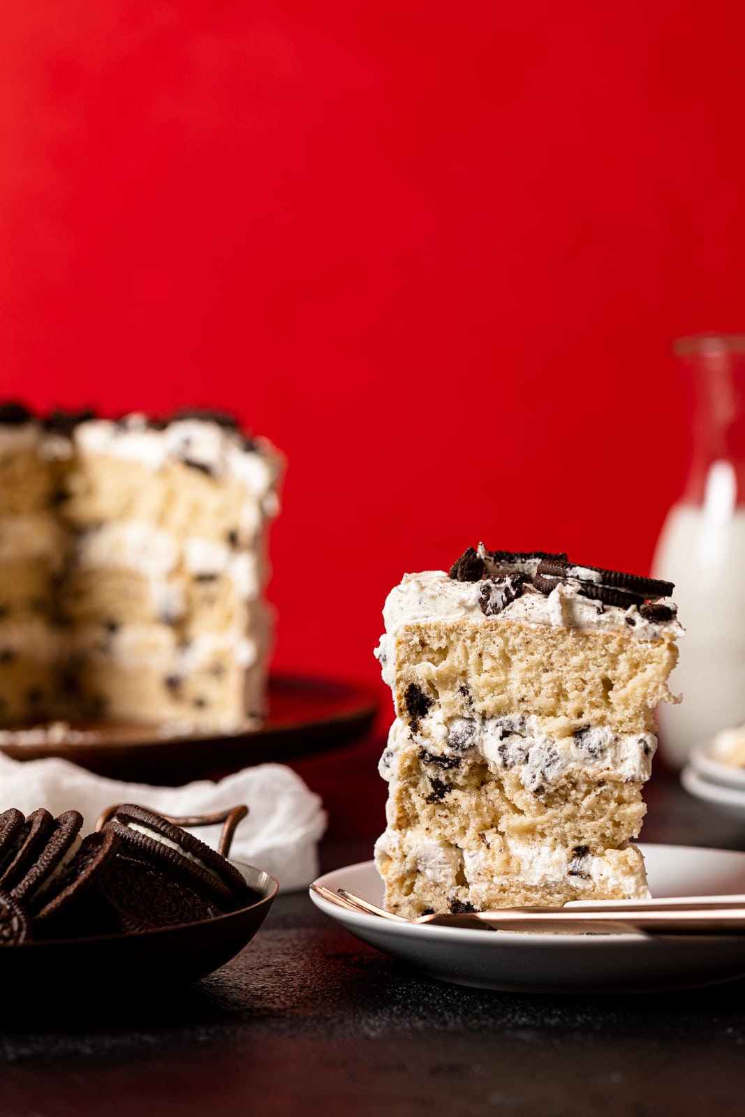 Slice of Vegan Vanilla Oreo Cake next to a bowl of Oreos